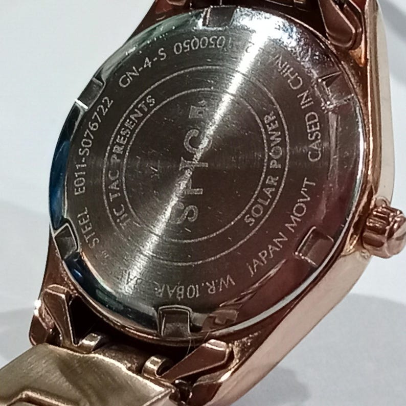Puede incluir: Primer plano de un reloj de pulsera de oro rosa. La parte trasera del reloj es visible, mostrando texto que incluye "STEEL", "JAPAN MOV'T" y "SOLAR POWER". El reloj est&aacute; marcado "W.R. 10BAR".