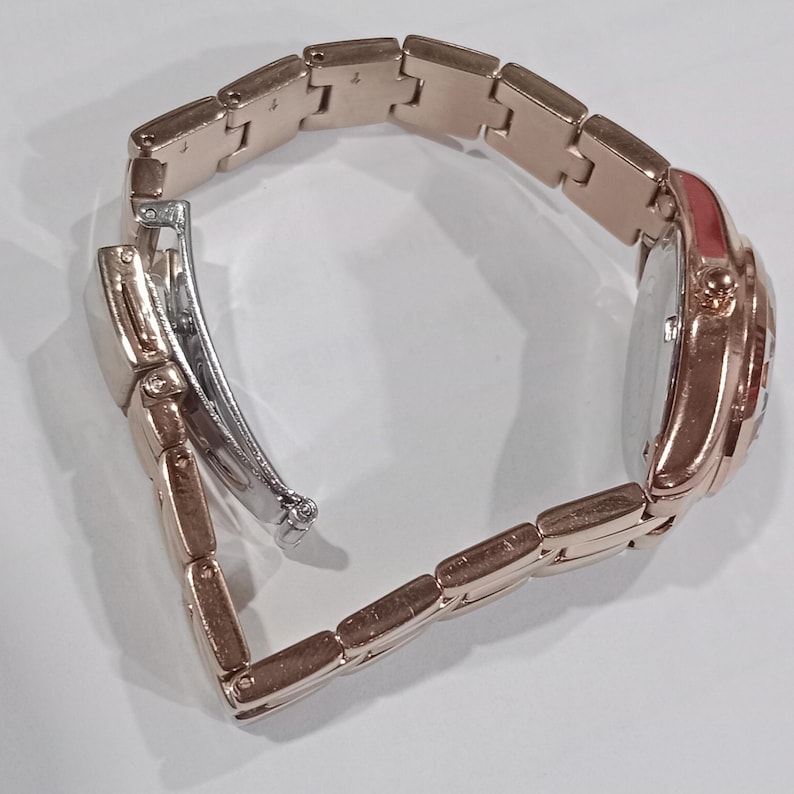 Puede incluir: Reloj de pulsera en tono oro rosa con cierre plateado. El reloj presenta una esfera redonda y una correa de eslabones. El reloj est&aacute; dise&ntilde;ado con una est&eacute;tica cl&aacute;sica, adecuado para el uso diario. La correa mide unos 18 cm de largo.
