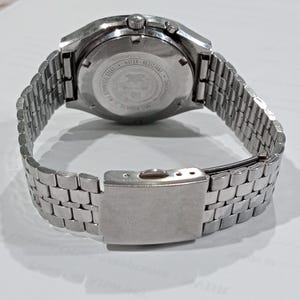 Puede incluir: Un reloj de pulsera de acero inoxidable en tono plateado con una correa de eslabones met&aacute;licos y un cierre desplegable. La parte posterior circular de la caja est&aacute; grabada con texto que incluye All Stainless Steel, Water-Resistant, Shockproof y Anti-Magnetic.