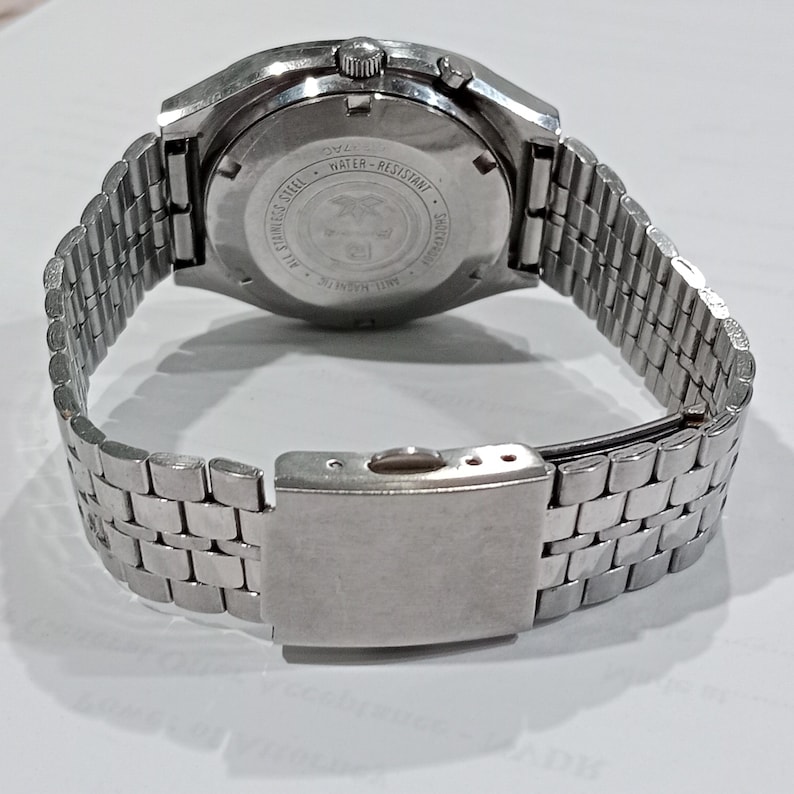Puede incluir: Un reloj de pulsera de acero inoxidable en tono plateado con una correa de eslabones met&aacute;licos y un cierre desplegable. La parte posterior circular de la caja est&aacute; grabada con texto que incluye All Stainless Steel, Water-Resistant, Shockproof y Anti-Magnetic.