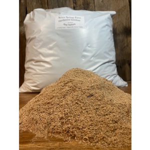 May include: A white bag filled with brown wood shavings. The bag is labeled "New Spring Farm Certified Organic Bedding for Small Animals".