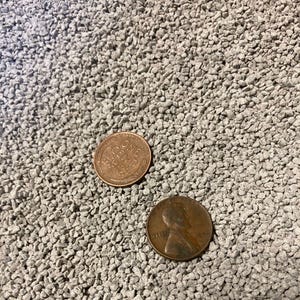 May include: Two copper pennies on a gray, textured surface. One penny shows the words "ONE CENT" and "UNITED STATES OF AMERICA". The other penny has a profile of a person and the year 1928.