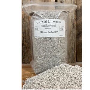 May include: A clear plastic bag filled with horticultural limestone. The bag has a white label with the text "CactiCal Limestone Horticultural - All Natural - Calcium Carbonate". A pile of the limestone is in front of the bag.