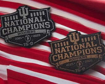May include: Two black and brown patches with the text "NATIONAL CHAMPIONS HOOSIERS 2025 16-0" are displayed against a red and white striped background. The patches have a shield shape with a university logo at the top.