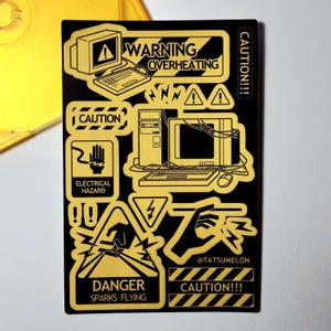 May include: A rectangular black sticker sheet featuring yellow graphic designs of vintage computer equipment and industrial warning signs. Text includes WARNING OVERHEATING, CAUTION, ELECTRICAL HAZARD, DANGER SPARKS FLYING, and @TATSUMELON.