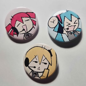 Puede incluir: Tres botones redondos con ilustraciones de personajes de dibujos animados. Un botón tiene un fondo rosa con un personaje con pelo rojo. Otro tiene un personaje azul y gris. El tercer botón tiene un personaje con pelo amarillo.