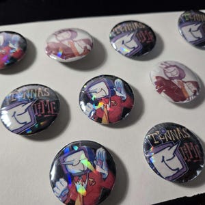 Puede incluir: Un conjunto de botones redondos y ovalados con un diseño de personaje de dibujos animados. El personaje tiene una cabeza con forma de televisor y viste un traje rojo. Algunos botones muestran el texto "TENNA'S TIME". Efecto holográfico.