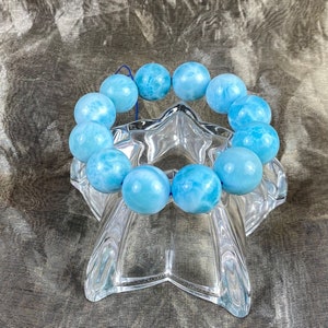 May include: A light blue gemstone bracelet with round beads. The bracelet is displayed on a clear glass star-shaped stand.