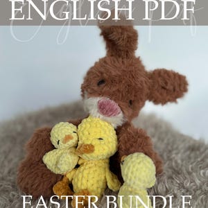 Op de afbeelding: Een bruin gehaakt konijn met een roze neus en drie gele gehaakte eendjes. De afbeelding heeft de tekst "Crochet Pattern ENGLISH PDF EASTER BUNDLE". Het konijn en de eendjes liggen op een zacht, grijs oppervlak.