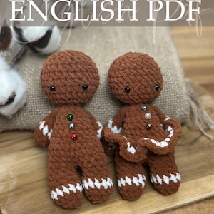 Op de afbeelding: Twee bruine gehaakte peperkoekmannetjes met witte glazuurdetails en knoopaccenten. De tekst "Crochet Pattern ENGLISH PDF" staat bovenaan de afbeelding. De onderkant van de afbeelding toont de tekst "Designed by Mowres".