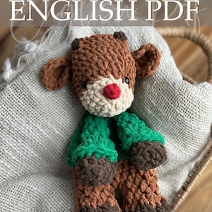 May include: A handmade crochet reindeer plushie with brown, green, and tan yarn. The reindeer has a red nose, black eyes, and the text "Crochet Pattern ENGLISH PDF". The plushie is sitting in a woven basket.