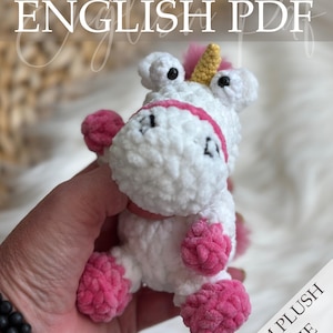 May include: A white and pink plush unicorn with a yellow horn and black eyes. The crochet unicorn is held in a hand. The text "Crochet Pattern ENGLISH PDF" is at the top of the image. The text "PALM PLUSH SERIE" is on the right side.