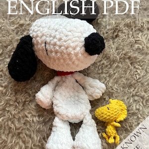 Op de afbeelding: Een grote, witte en zwarte Snoopy-knuffelpop met een rode kraag en een kleinere gele Woodstock-pop. De afbeelding bevat de tekst "Crochet Pattern ENGLISH PDF" en "WELL KNOWN SERIE". De poppen staan op een getextureerd, lichtbruin oppervlak.