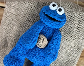 Op de afbeelding: Een handgemaakte blauwe Cookie Monster-pop van gehaakt garen met een beige gehaakte koekje. De pop heeft grote witte ogen met zwarte pupillen. De woorden "Crochet Pattern ENGLISH PDF" staan bovenaan de afbeelding.