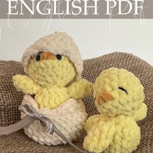 Op de afbeelding: Twee gehaakte gele kuikens, waarvan één in een crèmekleurige eierschaal met een zilveren lint. De tekst "Crochet Pattern ENGLISH PDF" staat bovenaan. De kuikens hebben zwarte ogen en oranje snavels.