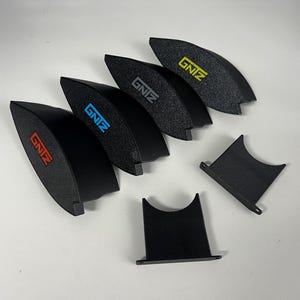 Puede incluir: Cinco piezas de plástico negro con forma curva y la palabra "GNZ" en diferentes colores en cada pieza. Dos piezas de plástico negro con forma rectangular.