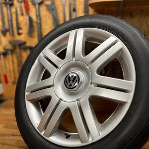 Könnte beinhalten: Ein silbernes Alurad mit einem schwarzen Reifen und einem Volkswagen-Logo in der Mitte.