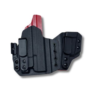May include: Black and red holster with two black clips and multiple screw attachments. The holster has a textured surface and a red accent on the top. The design includes several eyelets for adjustable retention.