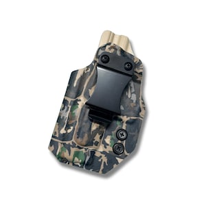 Puede incluir: Funda con estampado de camuflaje con un clip y herrajes de metal negro. La funda presenta una sección superior de color madera y está diseñada para un transporte seguro. El diseño de camuflaje incorpora tonos de verde, marrón y beige.