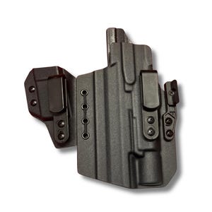 May include: A black, molded polymer holster with three metal belt clips. The holster has a textured surface and is designed to be worn on the body. The holster has a series of eyelets for attaching accessories.