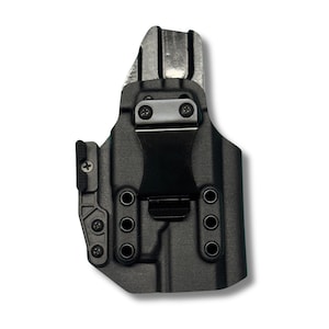 Op de afbeelding: Zwarte polymeer holster met een metalen clip en hardware. De holster heeft een gegoten ontwerp met meerdere schroefgaten en een getextureerd oppervlak. De clip is gecentreerd en vastgezet met twee schroeven. Ontworpen om een vuurwapen te houden.
