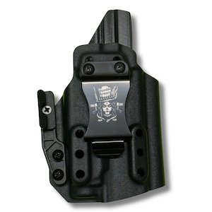 Op de afbeelding: Een zwarte gevormde holster met een metalen riemclip voorzien van het Voodoo Armory-logo en een schedelafbeelding. De holster bevat een verstelbaar zijhulpstuk vastgezet met schroeven, meerdere montagegaten en een textuur op het buitenoppervlak.