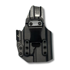 Op de afbeelding: Zwarte polymeer holster met een metalen clip en hardware. De holster heeft een gegoten ontwerp met meerdere schroefgaten en een getextureerd oppervlak. De clip is gecentreerd en vastgezet met twee schroeven. Ontworpen voor een vuurwapen.