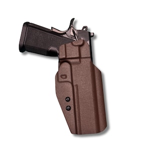 May include: A brown polymer holster with a black handgun. The holster has a textured surface and two black screws. The handgun is partially inserted into the holster, showing the grip and trigger.