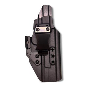 Puede incluir: Un letrero de madera rústico blanco con la palabra "Welcome" escrita a mano. El letrero tiene un aspecto envejecido y un elemento floral decorativo. El fondo es una imagen borrosa de una casa.