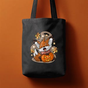 May include: Black tote bag with a cartoon fox and a carved pumpkin. The fox is brown and white, wearing a red scarf, and surrounded by autumn leaves and stars. The pumpkin is orange with a carved face.