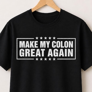 May include: A black short-sleeved t-shirt featuring a white rectangular graphic with the text "MAKE MY COLON GREAT AGAIN" centered in capital letters, flanked by five small stars above and five small stars below the text, all on a black background.