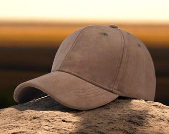 May include: A brown suede baseball cap with a curved brim. The cap is sitting on a rock.