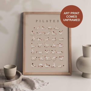 Peut inclure: Une affiche encadr&eacute;e avec un cadre en bois brun clair. L'affiche pr&eacute;sente un fond beige avec des illustrations d'une personne effectuant diff&eacute;rents exercices de Pilates. Le titre "PILATES" est imprim&eacute; en noir en haut de l'affiche. Le texte "ART PRINT COMES UNFRAMED" est imprim&eacute; en blanc sur un cercle brun dans le coin sup&eacute;rieur droit de l'image.