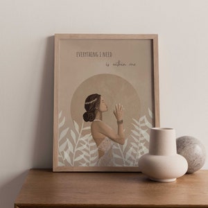 May include: A framed art print featuring a woman in a white dress with the text "EVERYTHING I NEED is within me." The artwork has a neutral color palette with beige and brown tones, and is decorated with floral elements.