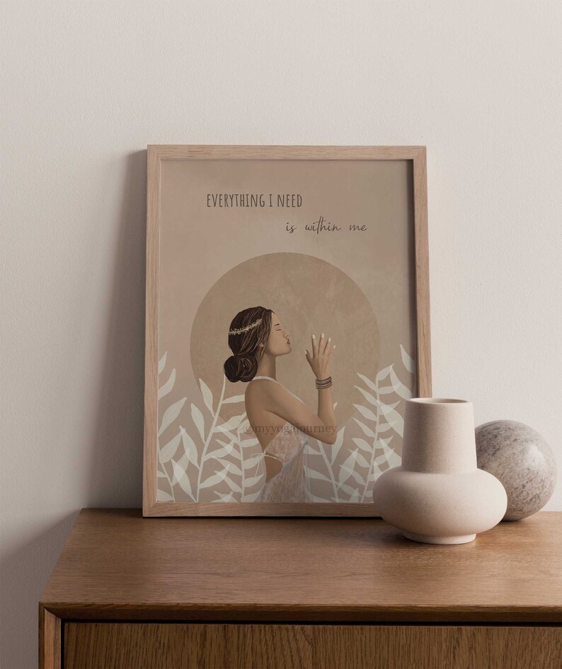 May include: A framed art print featuring a woman in a white dress with the text "EVERYTHING I NEED is within me." The artwork has a neutral color palette with beige and brown tones, and is decorated with floral elements.