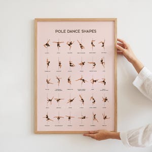 Könnte beinhalten: Ein gerahmtes Poster mit dem Titel "POLE DANCE SHAPES" zeigt Illustrationen verschiedener Pole-Dance-Posen. Das Poster hat einen hellrosa Hintergrund und einen Holzrahmen. Die Illustrationen zeigen Personen in schwarzen Outfits, die verschiedene Pole-Dance-Positionen demonstrieren.