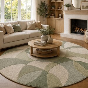 May include: A large, round area rug with a geometric pattern in shades of green and beige dominates the living room. A beige sofa with decorative pillows sits in front of a large window. A wooden coffee table and side table complete the cozy, inviting space.