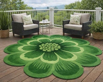 May include: A large, green, flower-shaped outdoor rug with varying shades of green. The rug is on a wooden deck, with two dark gray armchairs and a small side table. A white railing and greenery are in the background.
