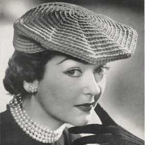 Könnte beinhalten: Ein Schwarzweißfoto einer Frau, die eine gehäkelte Baskenmütze trägt. Die Baskenmütze ist ein schlichtes Design mit einer abgerundeten Krone und einem flachen Rand. Die Frau trägt eine Perlenkette und Ohrringe.