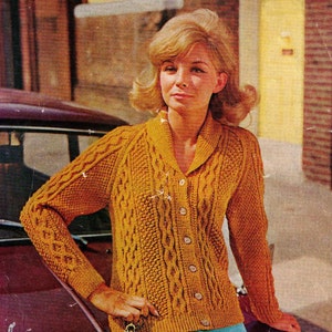 May include: Mustard yellow cable-knit cardigan with a shawl collar and button-down front. The long-sleeved sweater features textured patterns and is worn by a person. The cardigan is a vintage style.