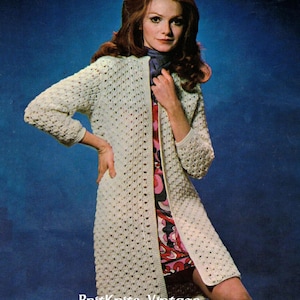 May include: A white crocheted cardigan with a long, open front and long sleeves. The cardigan is worn over a floral print dress.