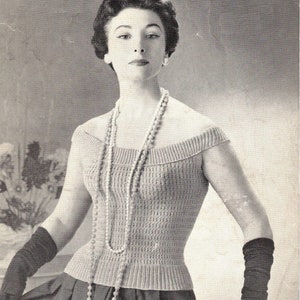 May include: A woman wearing a knitted off-the-shoulder top with a pearl necklace and black gloves.