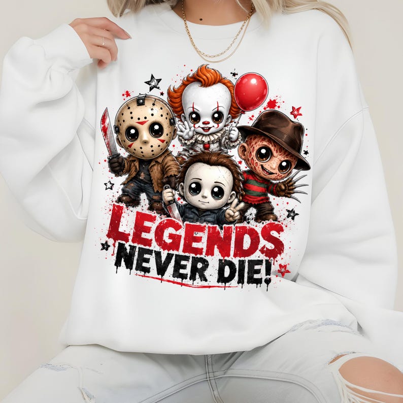 May include: A white long-sleeve sweatshirt featuring a graphic print of four chibi-style horror movie characters. Below the characters, the text reads "LEGENDS NEVER DIE!" in bold red and black lettering, accented by small black and red stars.