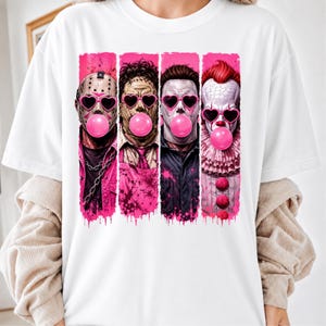 May include: A white t-shirt featuring a graphic print of four horror movie characters arranged in vertical panels. Each character wears pink heart-shaped sunglasses and blows a bright pink bubblegum bubble, set against a vibrant pink paint-splatter background.