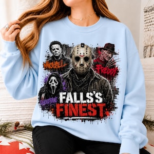 May include: A light blue crewneck sweatshirt featuring a graphic print of four horror movie characters: Michael, Jason, Freddy, and Ghostface. The text "FALLS'S FINEST" is printed in large red and white letters at the bottom of the graphic design.