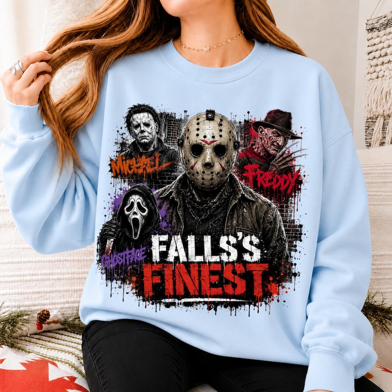May include: A light blue crewneck sweatshirt featuring a graphic print of four horror movie characters: Michael, Jason, Freddy, and Ghostface. The text "FALLS'S FINEST" is printed in large red and white letters at the bottom of the graphic design.