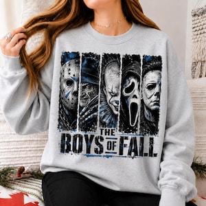 May include: A light grey crewneck sweatshirt featuring a graphic print of five horror movie characters arranged in vertical panels. Below the characters, the text reads THE BOYS OF FALL in bold, distressed black lettering with blue accents.