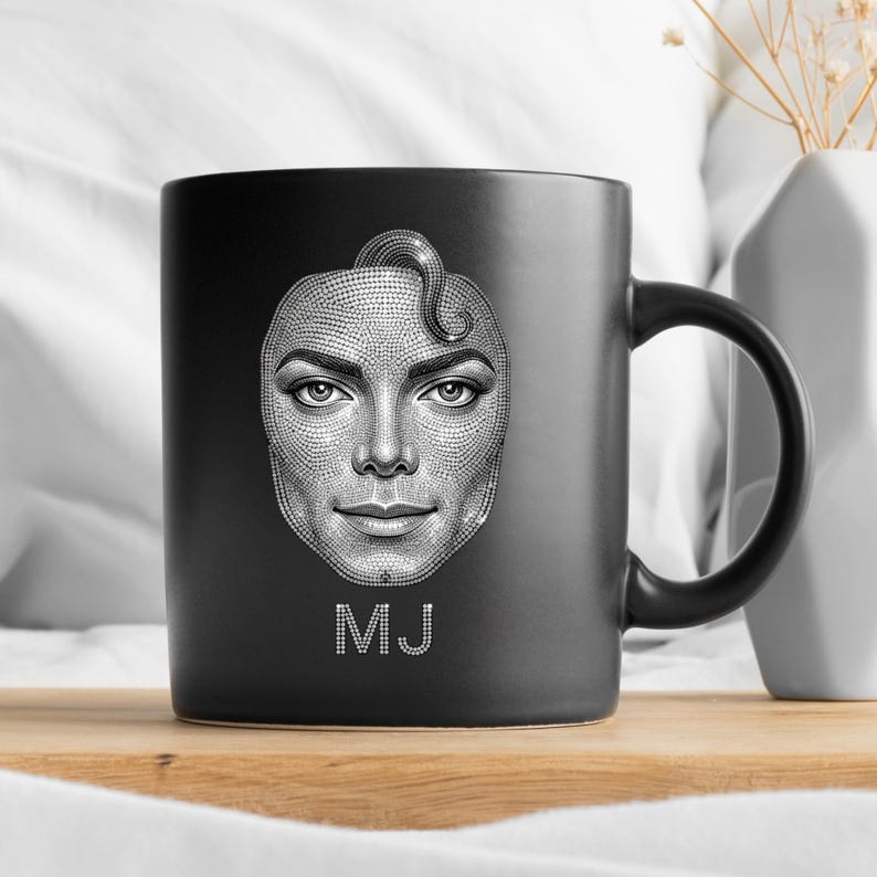 May include: Black ceramic mug featuring a detailed grayscale portrait of a person's face, with the initials "MJ" in white at the bottom. The mug has a black handle and is set against a neutral background.