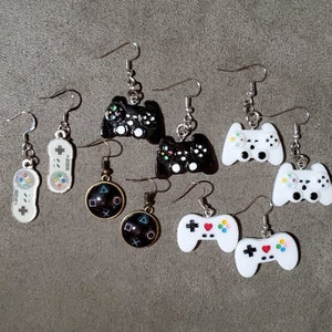 May include: Assortment of 10 video game controller earrings. The earrings are silver, gold, and black. The controllers are white, black, and gray. The earrings are shaped like different video game controllers.