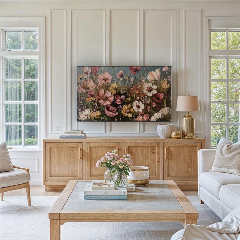 May include: A light wood cabinet with three doors and brass hardware. The cabinet is decorated with a floral painting above it. A coffee table with a glass top and a vase of flowers sits in front of the cabinet.